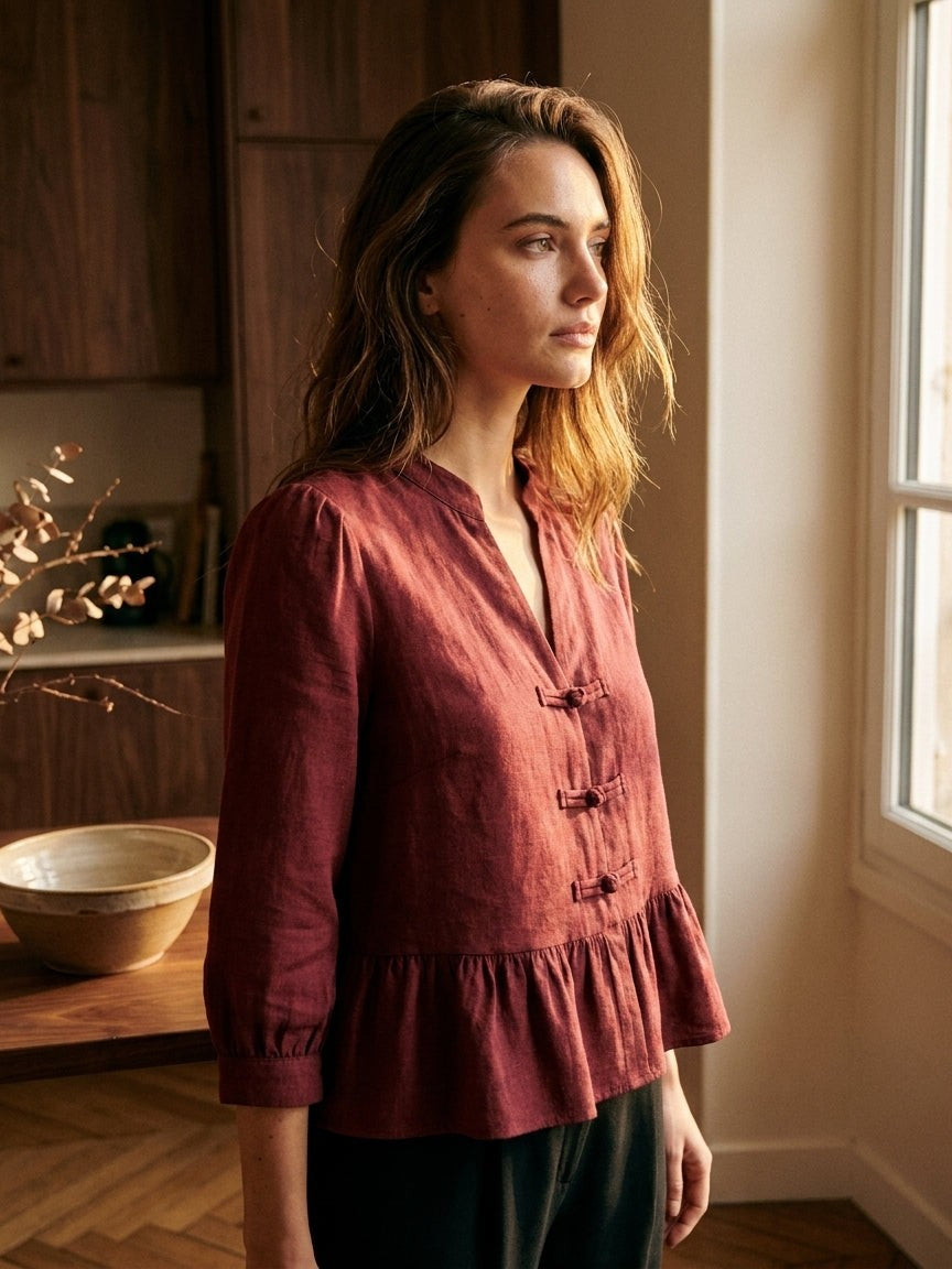 Woman in the Ycoo Emilie burgundy blouse with frog fastenings, in profile by a window